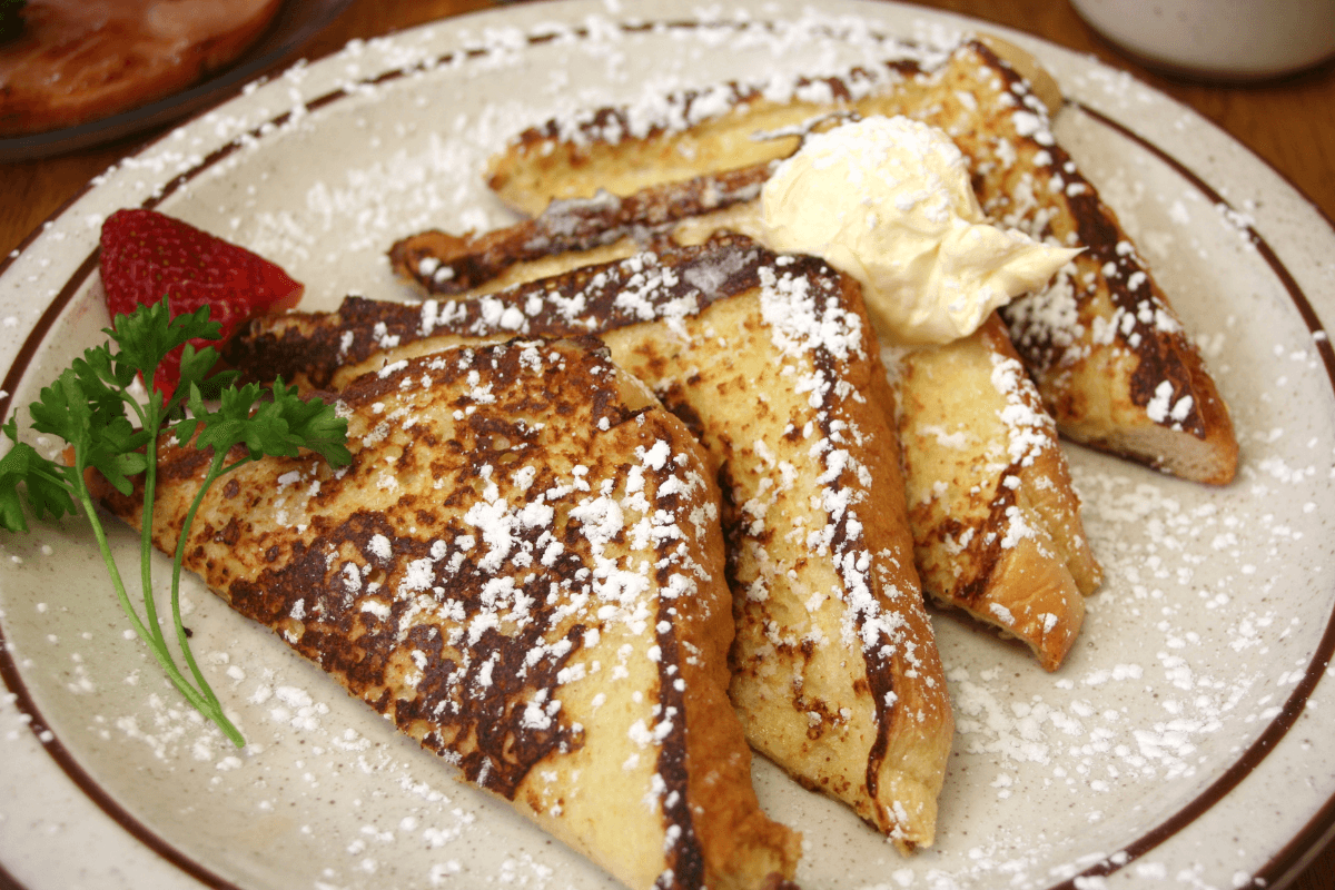 Biscuit French toast with powdered sugar, butter, and a strawberry garnish.