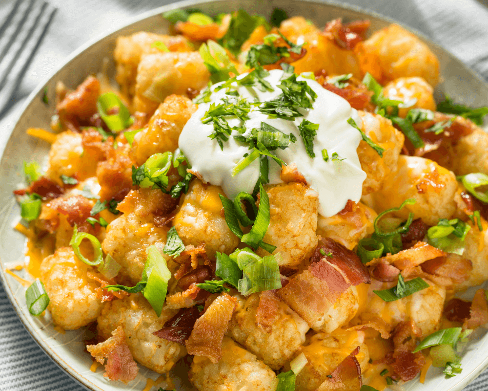 A bowl of cheesy tater tots topped with sour cream, and chopped green onions