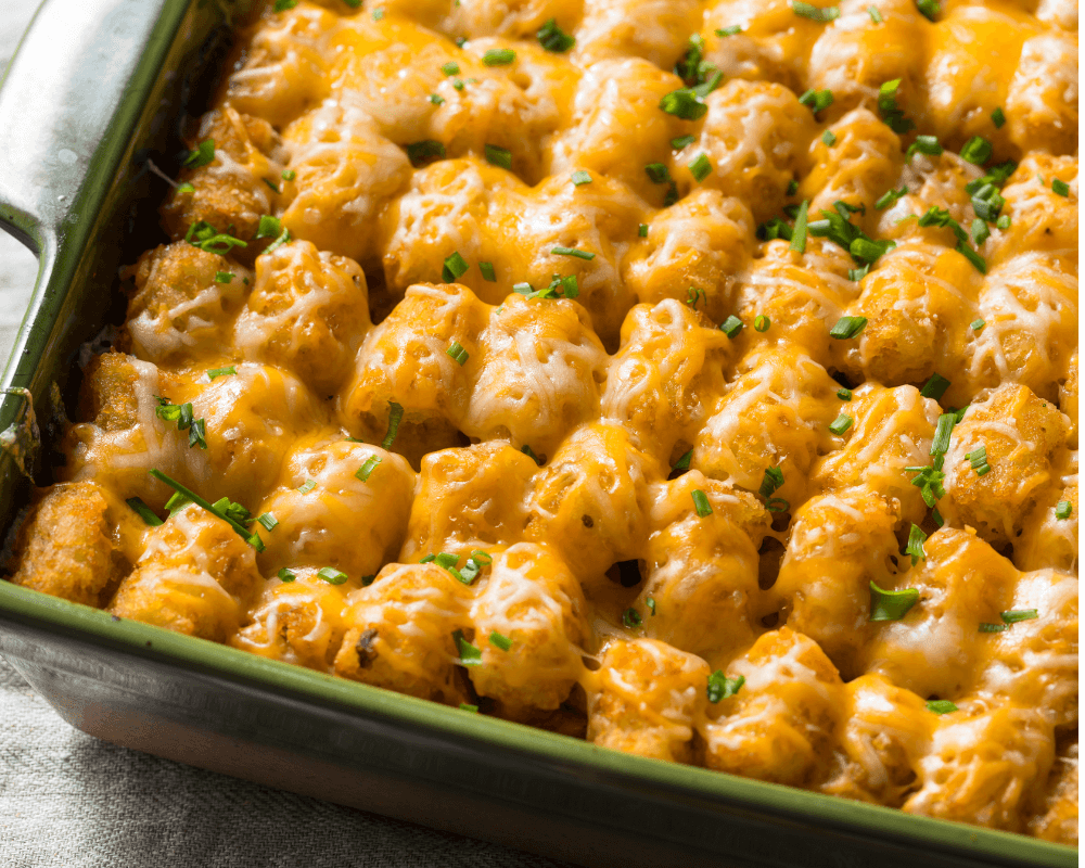 A baking dish filled with golden-brown Cheesy Tater Tots and sprinkled with chopped green herbs.