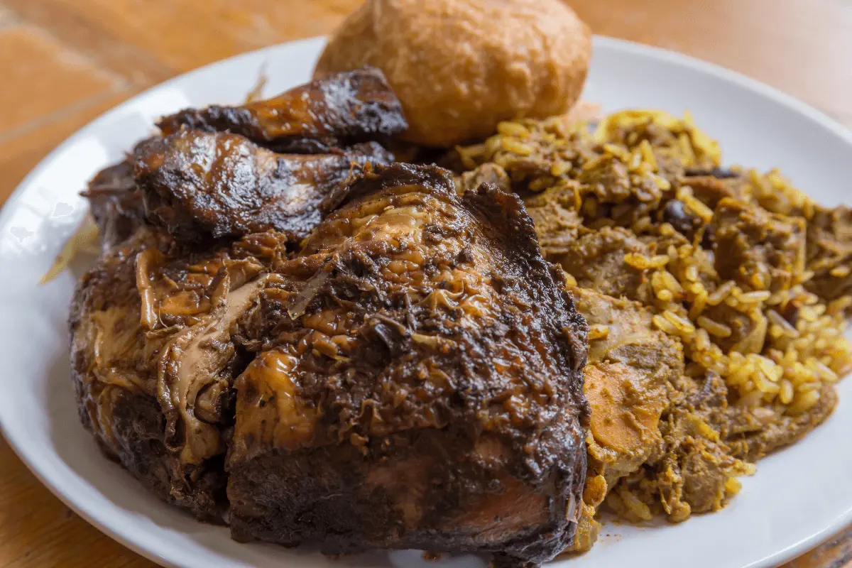 Jerk fried chicken with rice and a dumpling on a white plate.