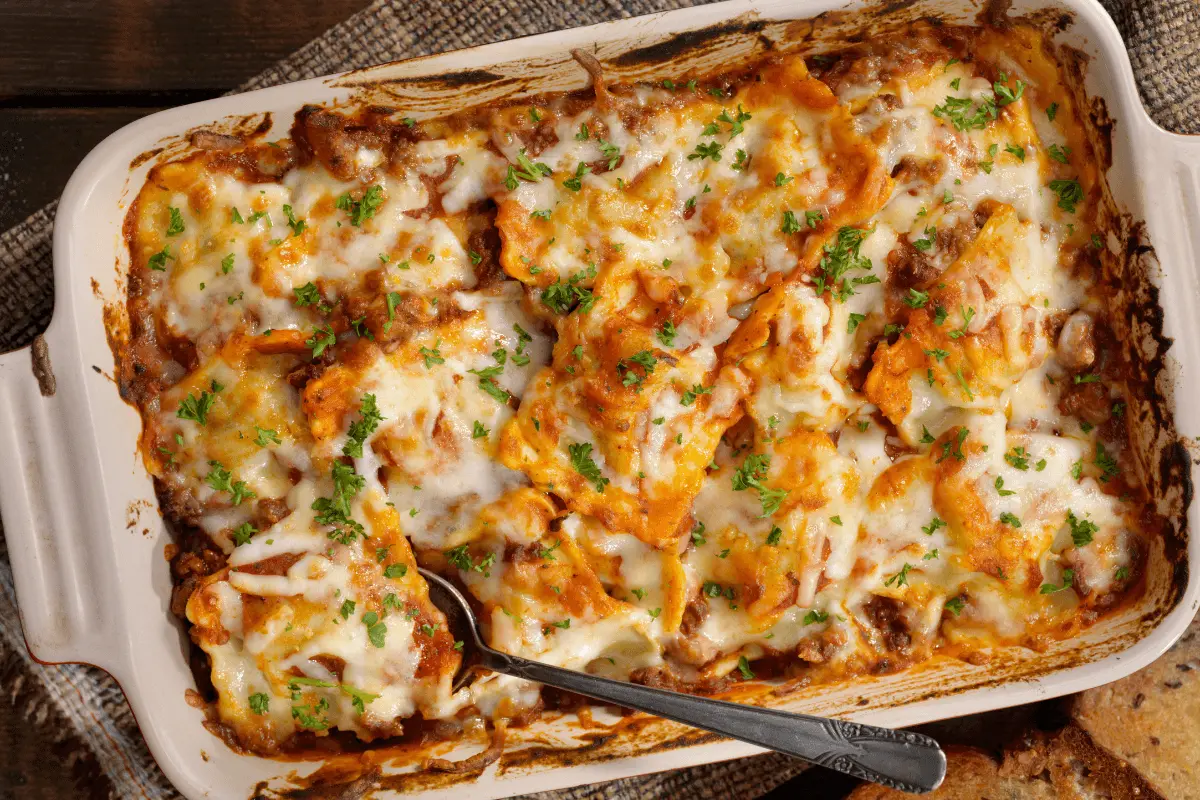 Baked lasagna with cream cheese topping, garnished with chopped parsley in a white casserole dish, showing layers of pasta, creamy cheese, and meat sauce.